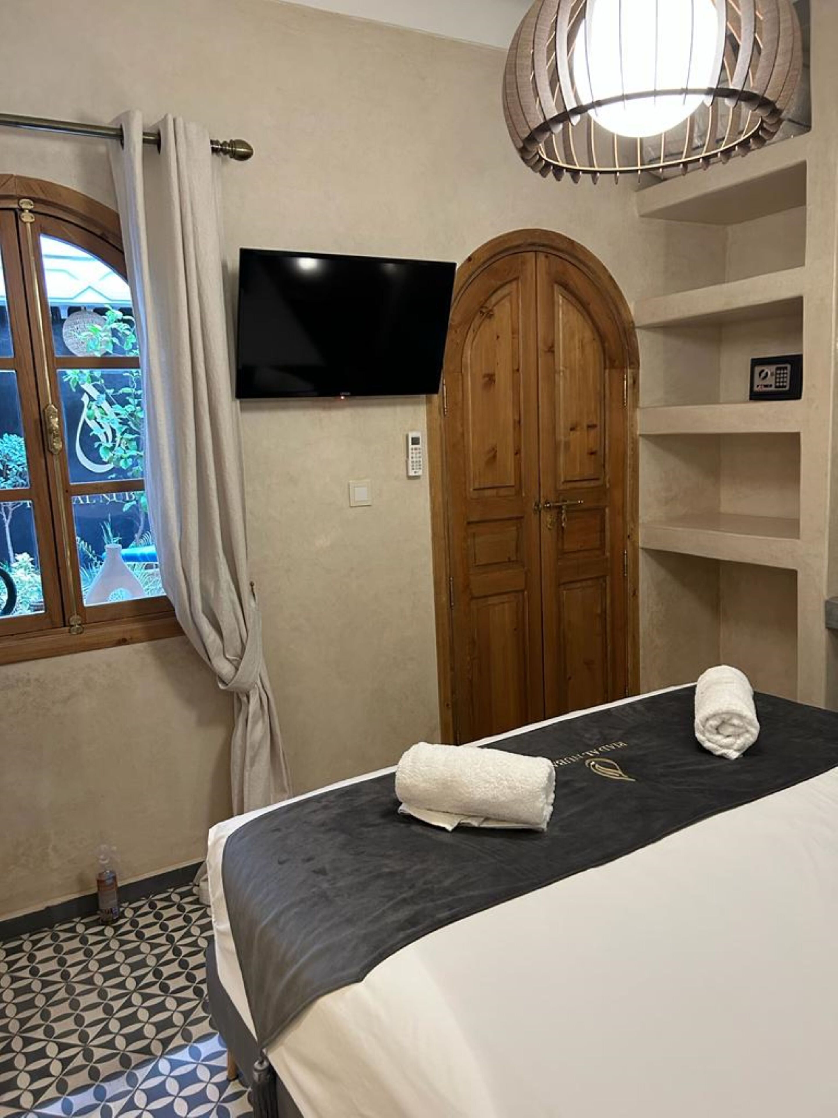Ein Hotelzimmer mit Bett, Fernseher, Holzschrank und einem fenster mit Vorhängen.