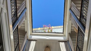 Une vue depuis un balcon, avec un ciel bleu dégagé visible à travers une fenêtre encadrée de balustrades en métal ouvragé.