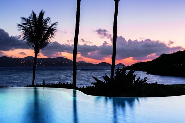 A pool with a sunset view, palm trees, and a calm sea. - Premier top floor location at tropical paradise Ritz Carlton Residence's. (St Thomas)