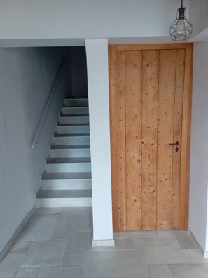 A staircase leading to a wooden door with a metal handle, white walls, and a hanging light fixture. - LE Passage 1 (Montaren-et-Saint-Médiers)