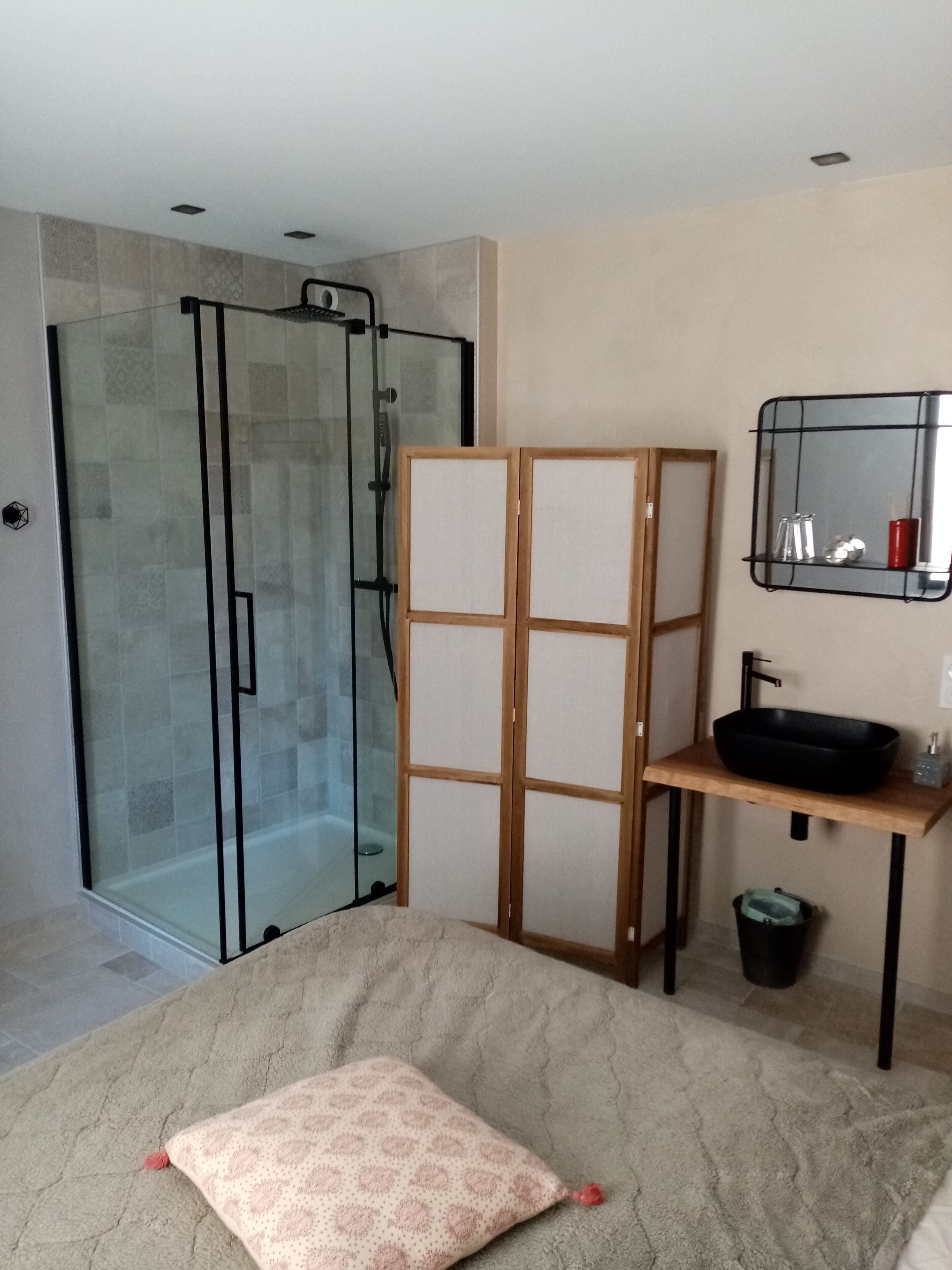 Un baño moderno con cabina de ducha de vidrio, mueble de madera, lavabo de cerámica negra y espejo con marco metálico.