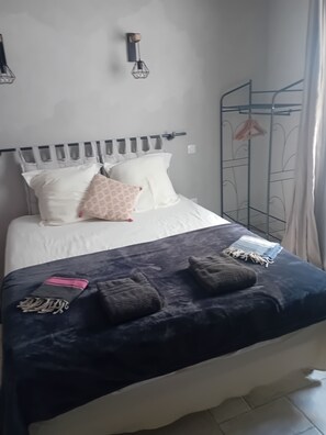 A bed with a dark blue blanket, two pillows, and a hanging clothes rack to the right. - LE Passage 1 (Montaren-et-Saint-Médiers)