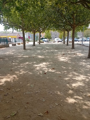 An outdoor area with trees, a basketball court, and parked cars.