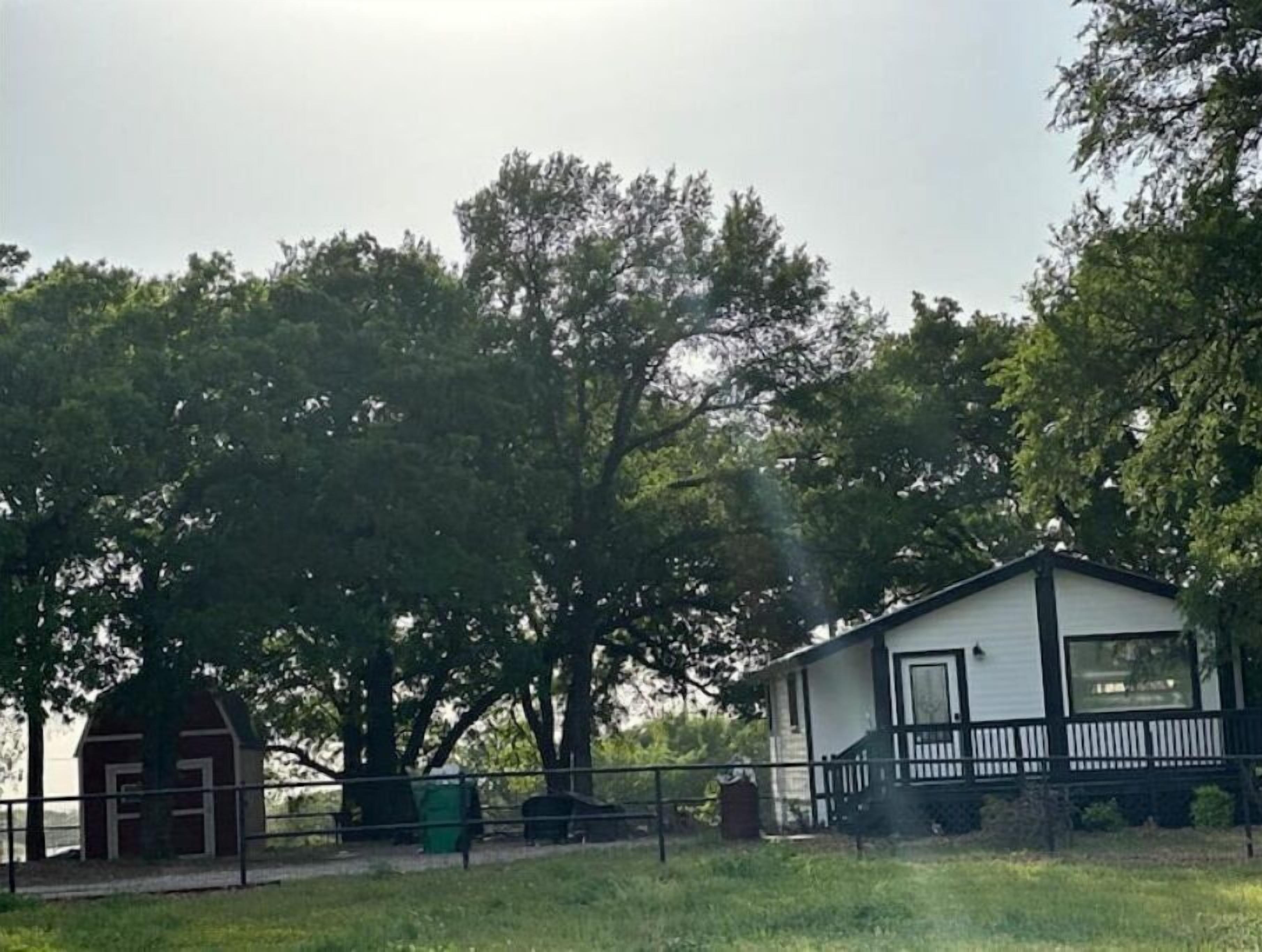 A small white house with a black porch and a red barn in the background.