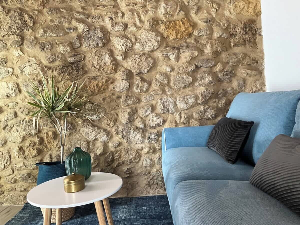 A living room with a stone wall, a blue sofa, a small round table with a plant, and a vase.