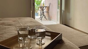 A bedroom with a bed, a bedside table with glasses and a tray, and an open door leading to a balcony with a table and chairs. - RUA 39 fine apartments 3 (Syracuse)