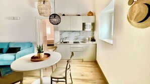 A modern kitchen with white cabinets, a marble backsplash, and a built-in microwave. There is a dining area with a white table and chairs, and a blue sofa in the background. - RUA 39 fine apartments 3 (Syracuse)