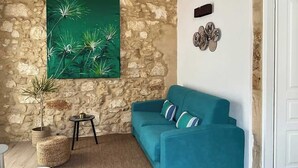 A living room with a stone wall, a teal sofa, a small round table, and a large green painting. - RUA 39 fine apartments 5 (Syracuse)