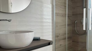 A modern bathroom with a large white vessel sink, a mirror, and a glass-enclosed shower area. - RUA 39 fine apartments 5 (Syracuse)