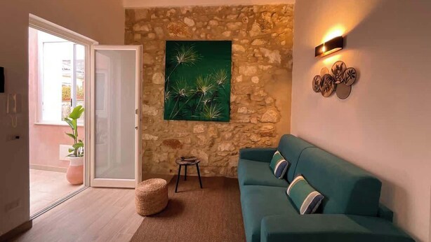 A cozy living room with a stone wall, a green painting, a teal sofa, and a small side table. - RUA 39 fine apartments 5 (Syracuse)