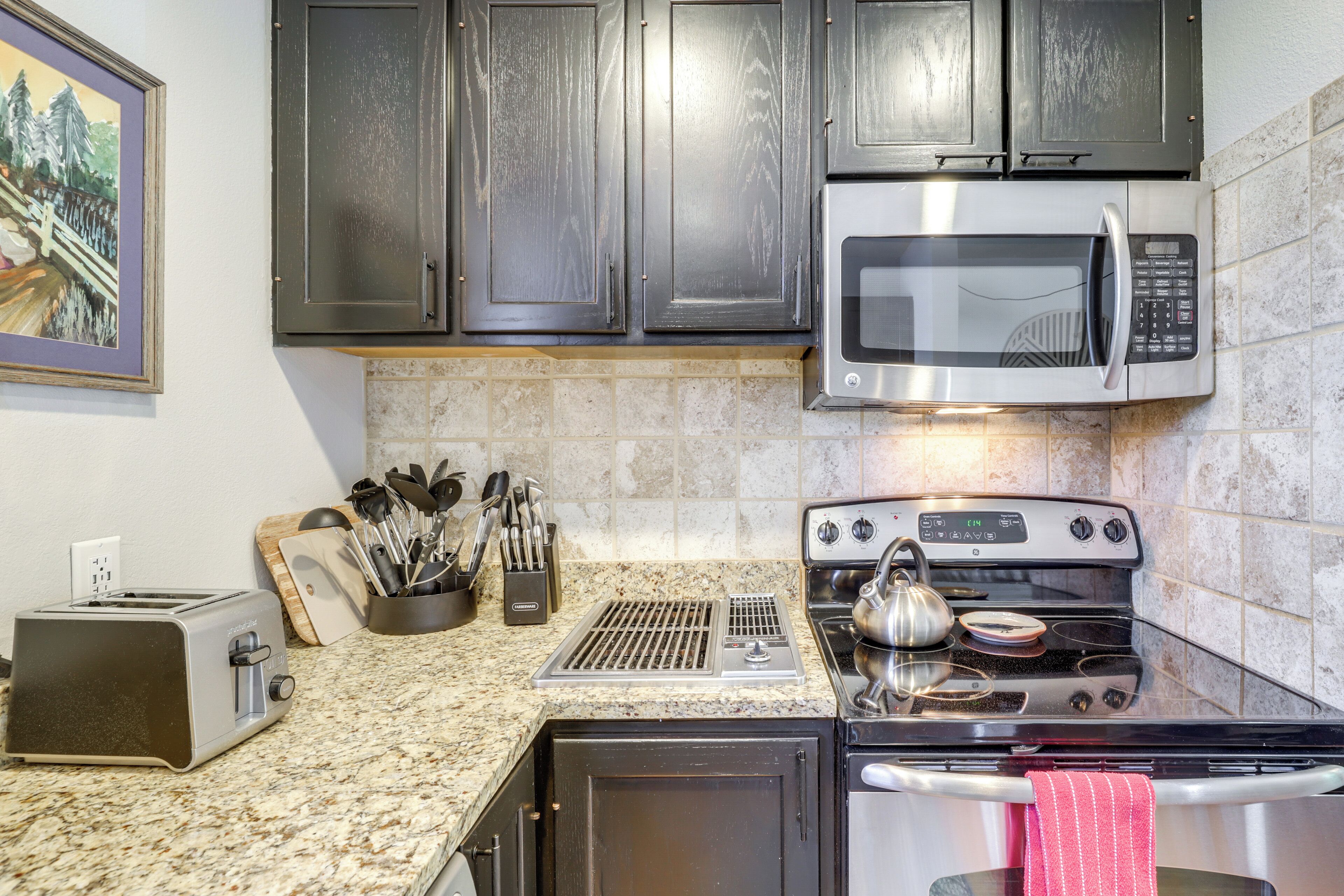 A kitchen with dark cabinets, a stainless steel microwave, a stove, and a toaster.