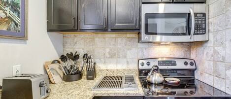 A kitchen with dark cabinets, a stainless steel microwave, a stove, and a toaster.
