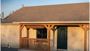 A building with a stone facade, a wooden porch with a railing, and a green door. - 2 minutes to downtown! Hill Country Luxury Duplex TX Wine Trail - Home B (Johnson City)