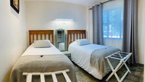 A room with two single beds, a small table, a mirror, and a window with curtains. - Mispa George - Self Catering Apartment - Sleeps 2 (George)