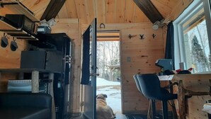 A wooden cabin interior with a kitchen area, a dining table, and a dog sitting by the door.