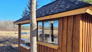 A wooden cabin with large windows, a sloped roof, and a view of a natural landscape.