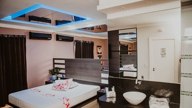 Una habitación de hotel moderna con una cama, mesita de noche y baño con lavamanos y espejo.