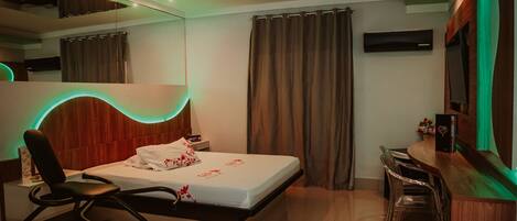 A modern hotel room with a bed, a desk, a chair, and a mirror.