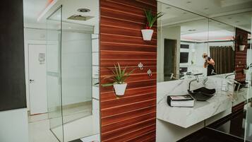 A modern bathroom with a glass shower enclosure, a marble countertop, and wooden paneling.
