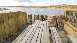 Eine Holzterrasse mit Blick auf einen Strand und ein Gewässer.