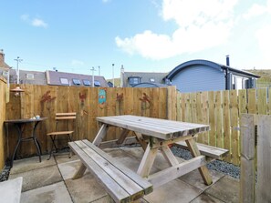 A wooden picnic table with benches, a small table, and a chair in a backyard with a wooden fence and houses in the background. - Shell Cottage (Peterhead)