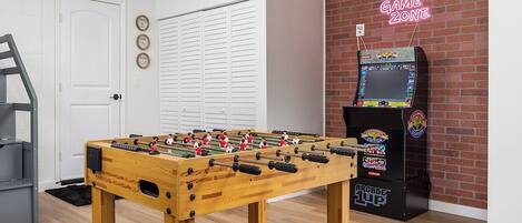 Una habitación con mesa de futbolín, mueble para futbolín y un letrero de neón que dice 'GAME ZONE'.
