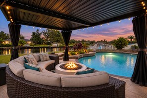A poolside area with a curved seating arrangement, a fire pit, and a view of a lake at dusk.