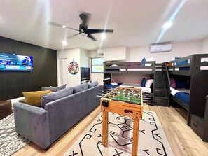 A room with a foosball table, bunk beds, a sofa, a dartboard, and a television.