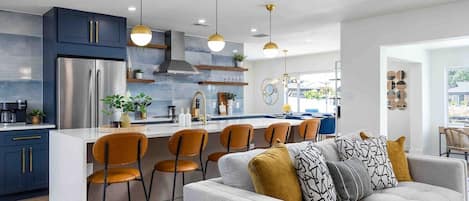 Une cuisine moderne dotée d’un îlot central, de tabourets de bar et de luminaires suspendus.