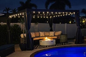 An outdoor seating area with a fire pit, string lights, and a pool.