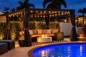 An outdoor pool area with a fire pit, seating, and string lights.
