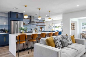 A modern kitchen with a central island, bar stools, and pendant lighting.