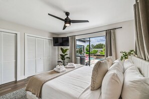 Ein Schlafzimmer mit Bett, Deckenventilator, Fernseher und Blick auf einen Außenpool.