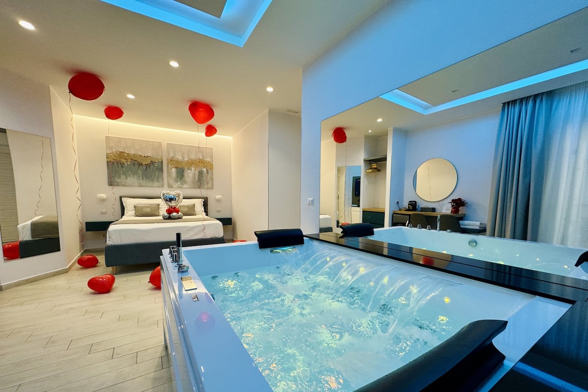 Une salle de bain moderne avec une grande baignoire, un miroir et un lit décoré d’un motif en forme de cœur.
