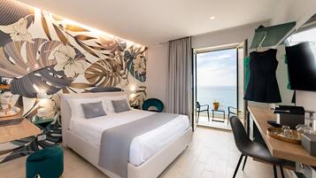 A modern hotel room with a large bed, a desk, and a view of the sea.