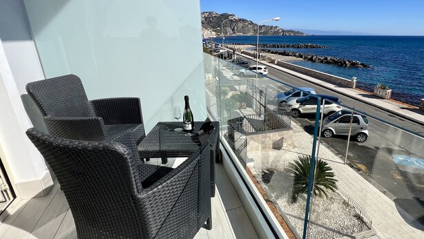 Un balcon agrémenté de meubles en osier, une bouteille de champagne et une vue dégagée sur la mer et une route côtière.