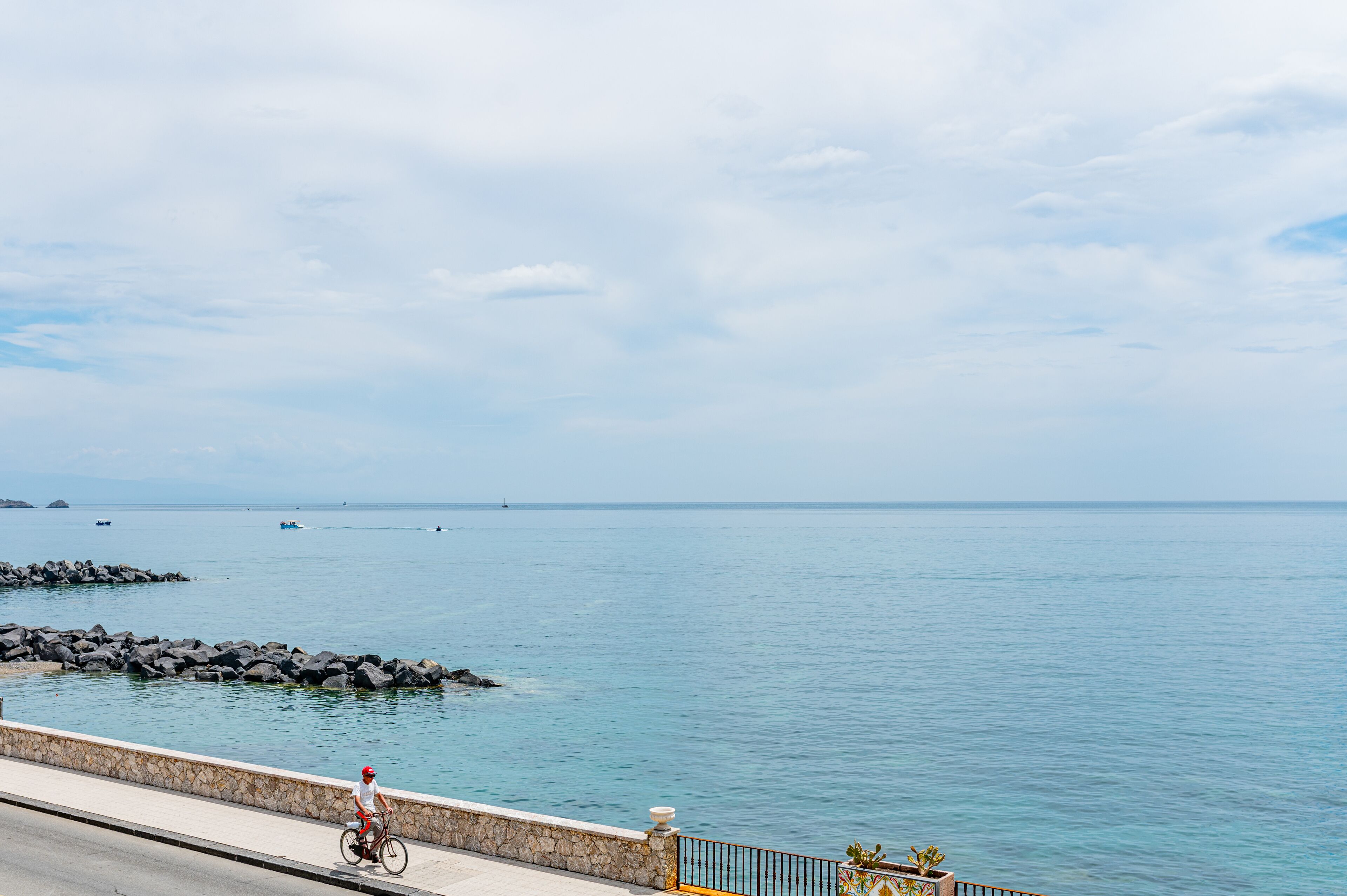 Une route côtière, un cycliste, un mur de pierres et une mer calme.