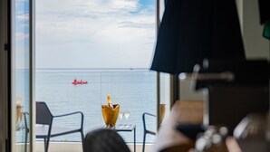 Une pièce avec vue sur la mer, une table avec une bouteille et des verres, et deux chaises.
