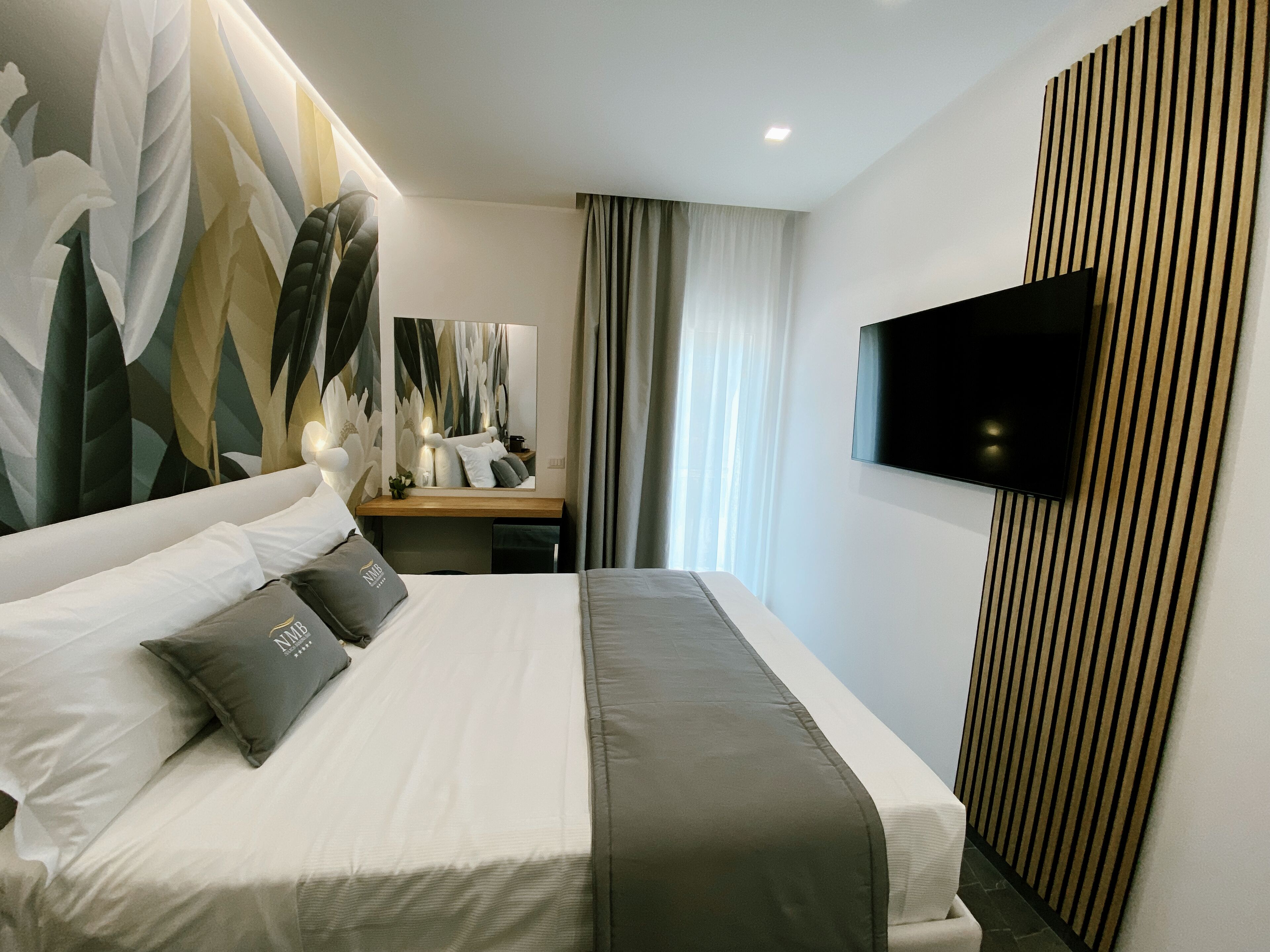 Una habitación de hotel moderna con una cama grande, un escritorio con silla, un televisor de pantalla plana en la pared y un panel decorativo.
