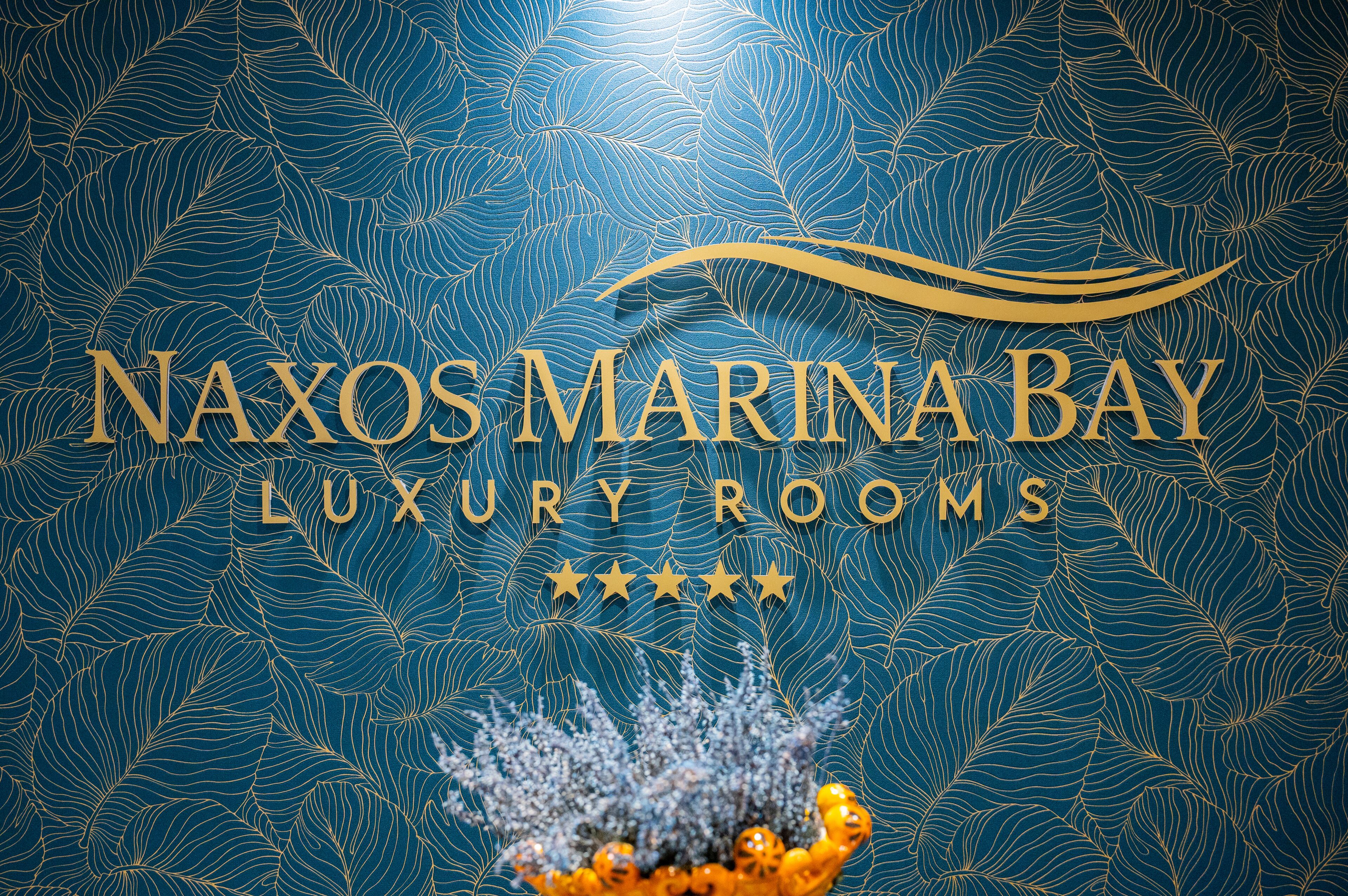 A logo for "NAXOS MARINA BAY LUXURY ROOMS" with a decorative leaf pattern and a decorative element at the bottom.