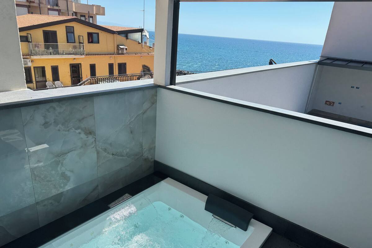 Une salle de bain moderne avec un jacuzzi entouré de parois en verre, des murs en marbre et une vue sur la mer.