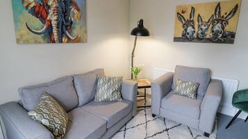 Een woonkamer met twee grijze banken, gestreepte kussens, een zwarte vloerlamp en twee schilderijen aan de muur.