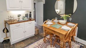 Un comedor con una mesa de madera dispuesta para cuatro personas, armarios blancos, una pared de acento oscura y un espejo grande.