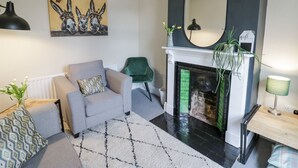 Una sala de estar con un sofá gris, un tapete estampado, una chimenea y un espejo grande.