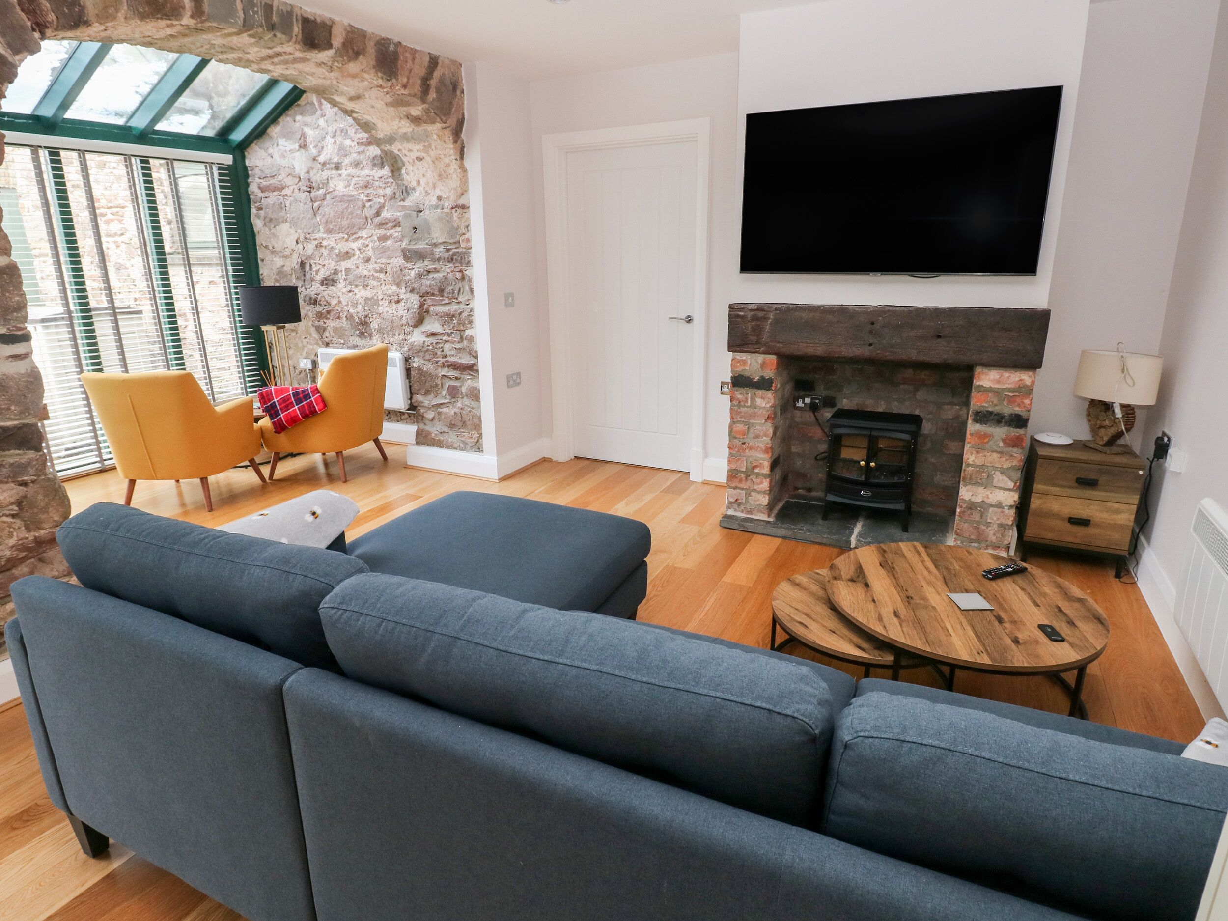 A living room with a stone wall, a fireplace, a TV, a sofa, and a yellow chair.
