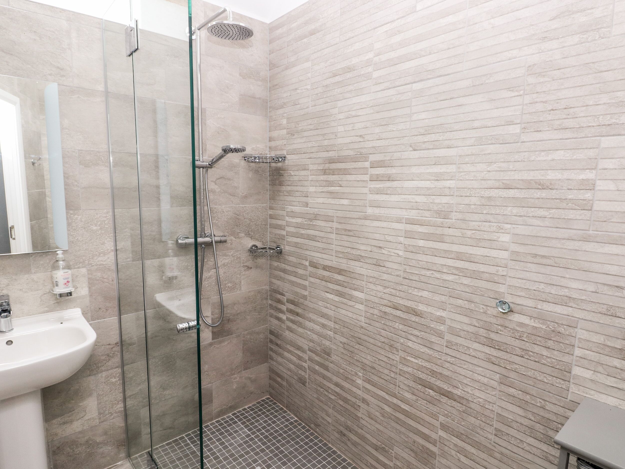 Ein modernes Badezimmer mit einer gläsernen Duschkabine, einem weißen Waschbecken und einer gefliesten Wand.