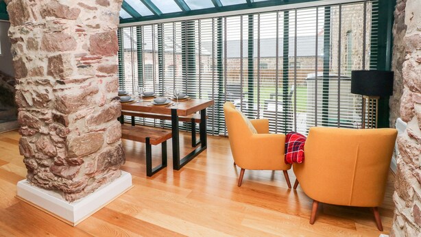 A dining area with a wooden table set for four, a stone column, and a yellow armchair.