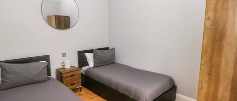 A bedroom with two beds, a wooden wardrobe, a bedside table, and a round mirror on the wall.