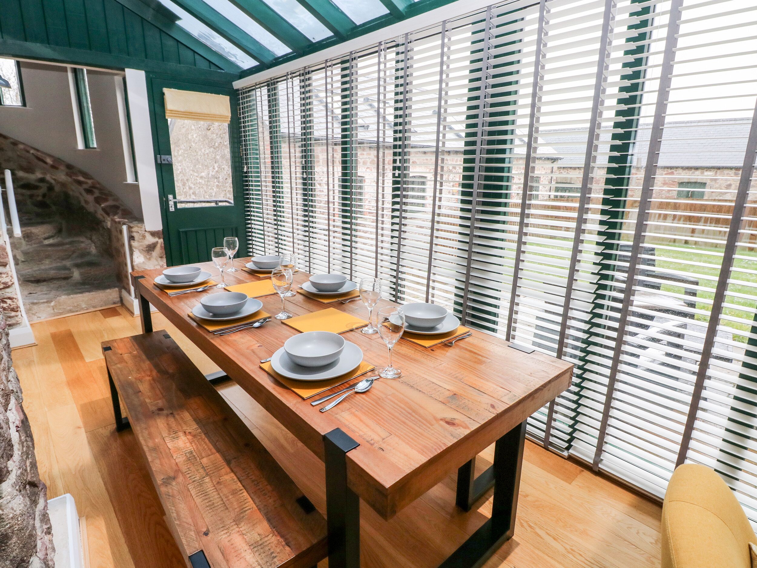 Un coin repas avec une longue table en bois dressée pour six personnes, agrémentée de bols gris et de verres à vin.