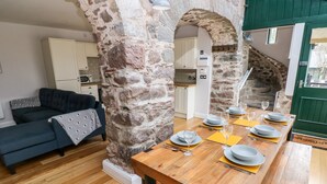 A dining area with a wooden table set for six, a sofa, and a stone wall.